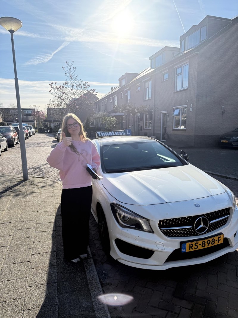 Geslaagde leerling in roze trui naast de lesauto