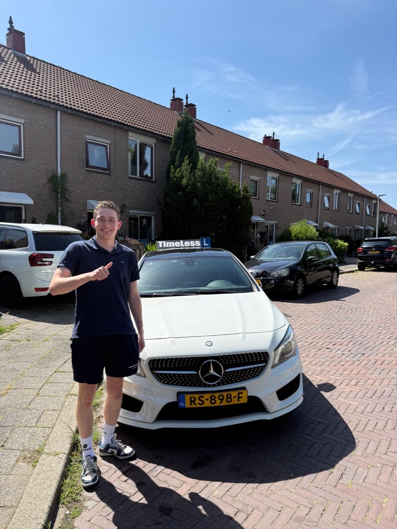Geslaagde leerling steekt zijn duim op naast de auto